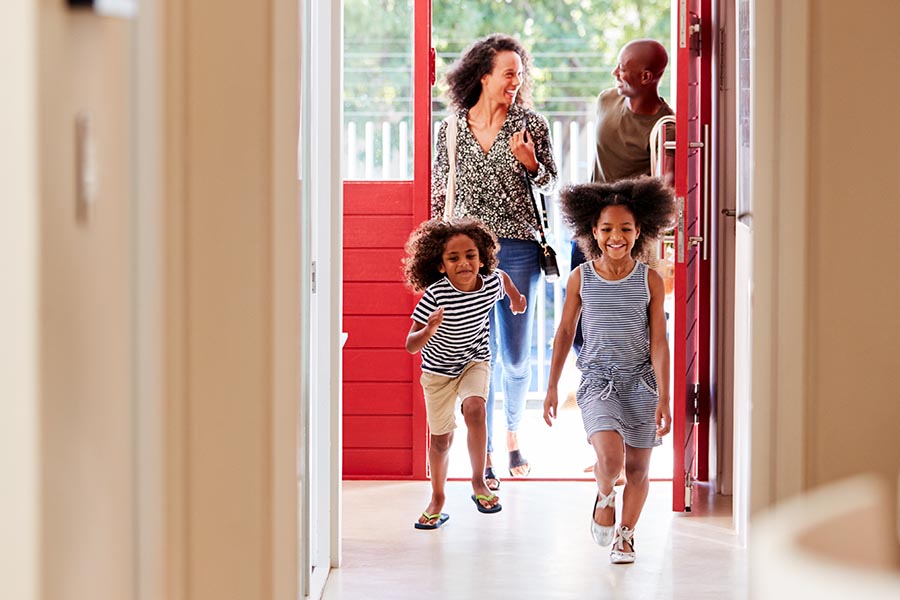 Blog - Family Returning Home, Parents Smiling, Kids Laughing and Running Through the Bright Red Door
