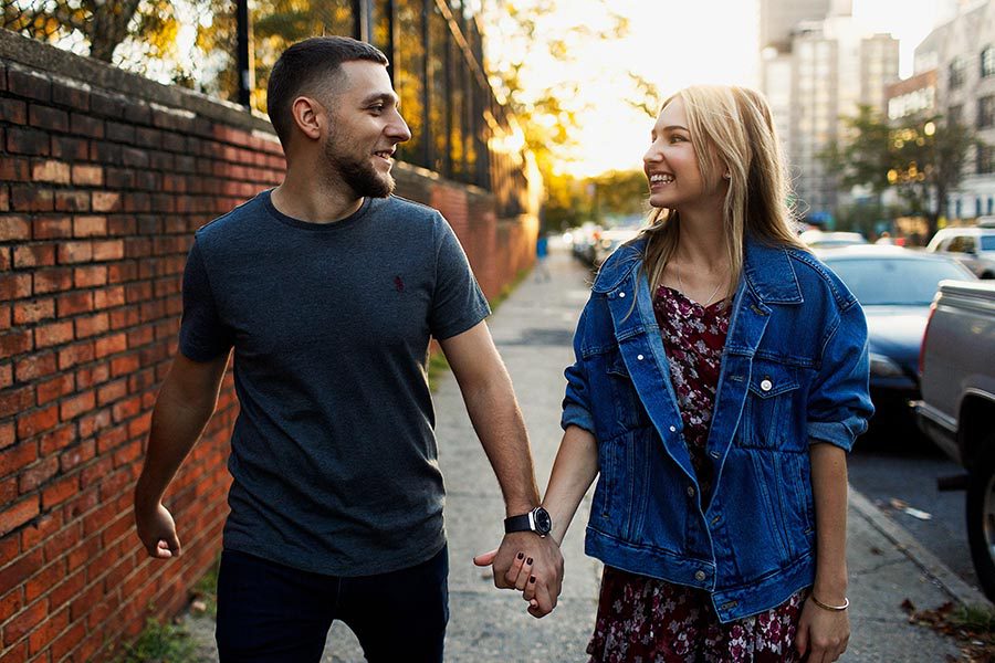 Client Center - Young Couple Holding Hands and Smiling At One Another, Walking Through the City